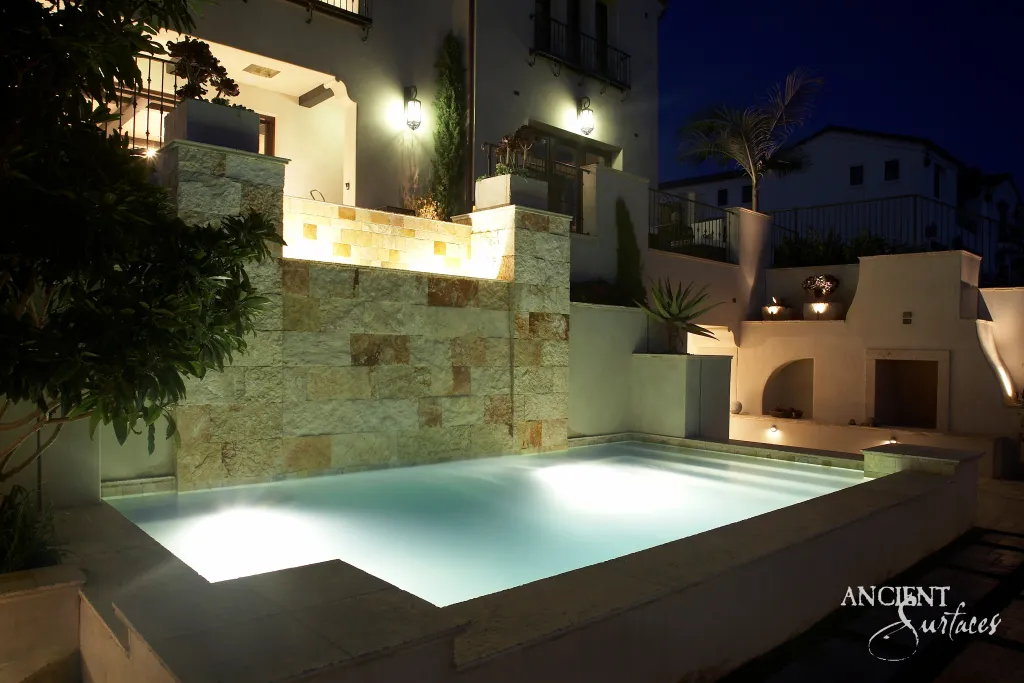 Reclaimed limestone pool cladding and coping illuminated at night below a terraced house