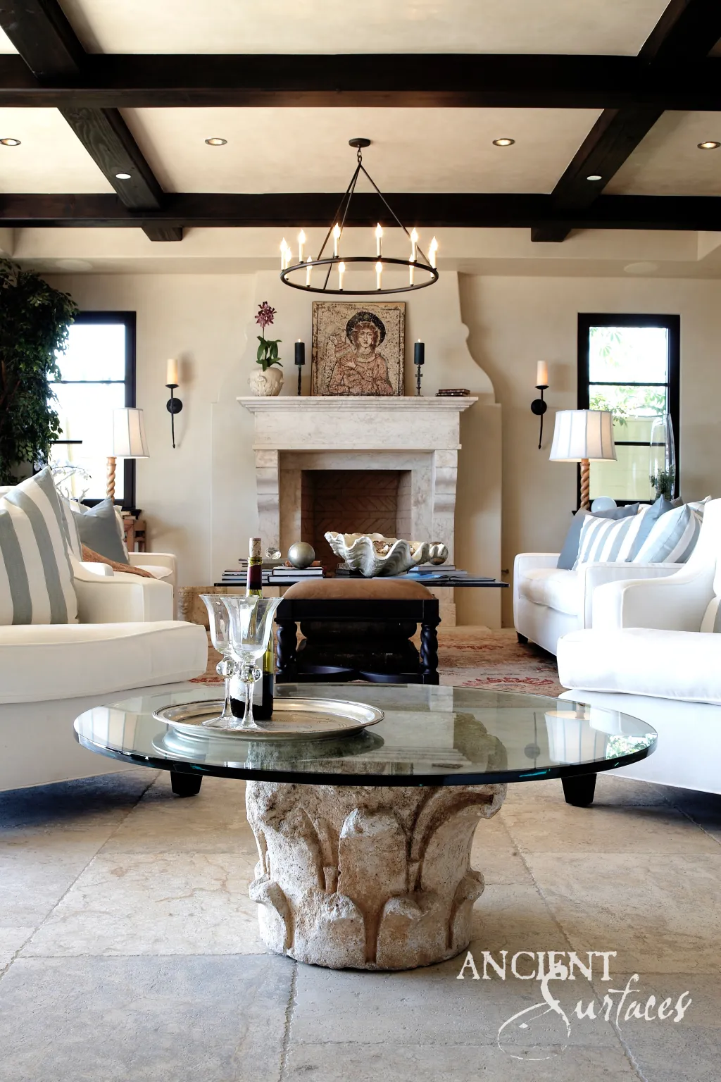 Reclaimed limestone fireplace mantel beneath a mosaic icon, with large limestone floor slabs and a carved stone capital supporting a glass coffee table