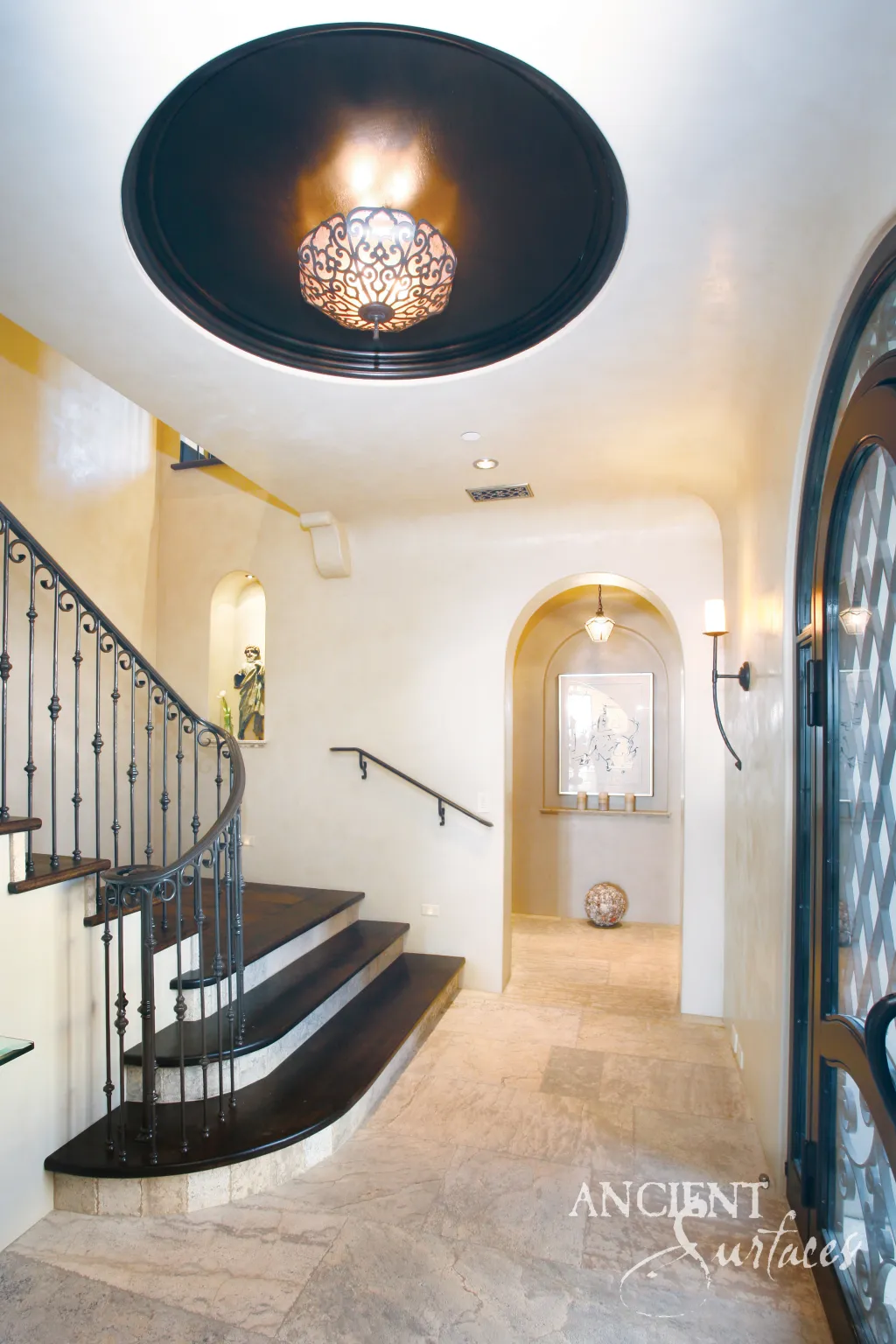 Entry foyer with limestone flooring running past a curved staircase with a scrolled iron railing toward an arched hallway