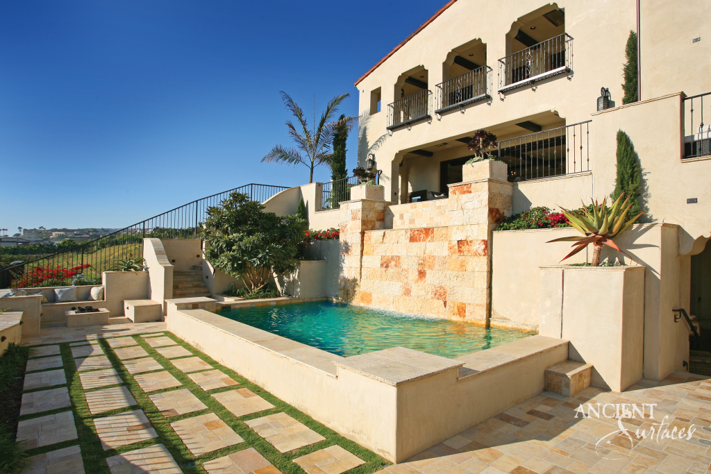 Pool framed by reclaimed limestone cladding and coping, with a sheet of water spilling from the limestone wall beside stone pavers set in grass