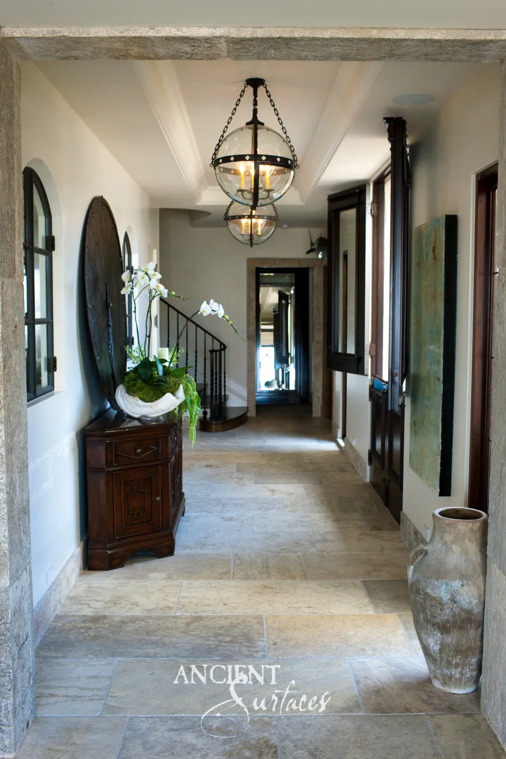 Reclaimed Dalle de Bourgogne limestone hallway floor laid in large worn slabs, seen through a stone doorway past a dark wooden console and orchids