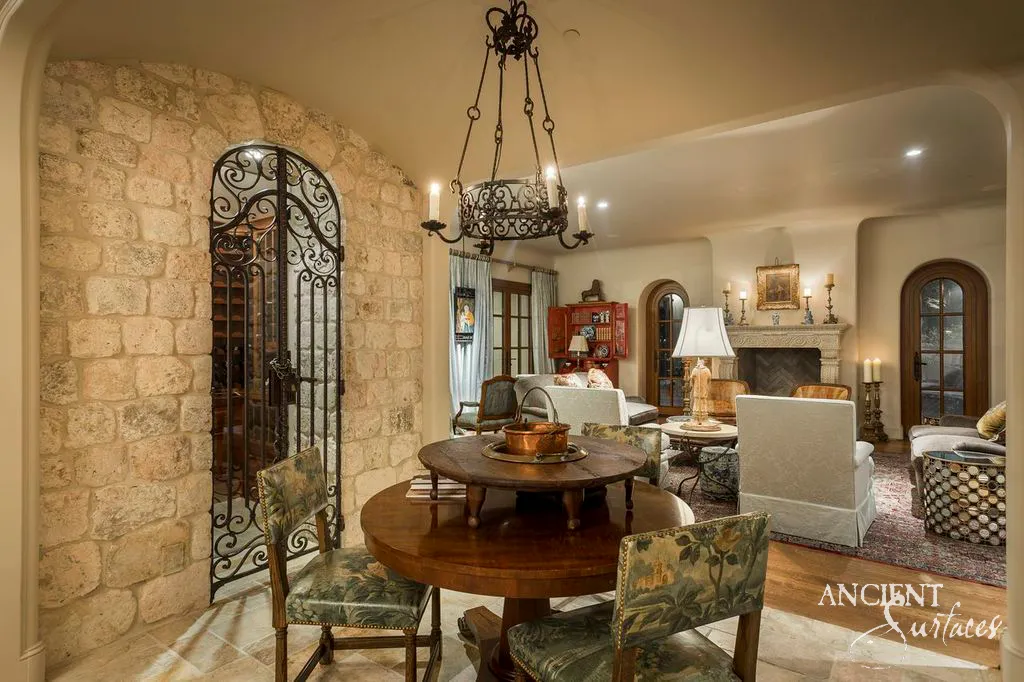 Arched wrought iron wine cellar door set into a curved wall of reclaimed antique limestone cladding