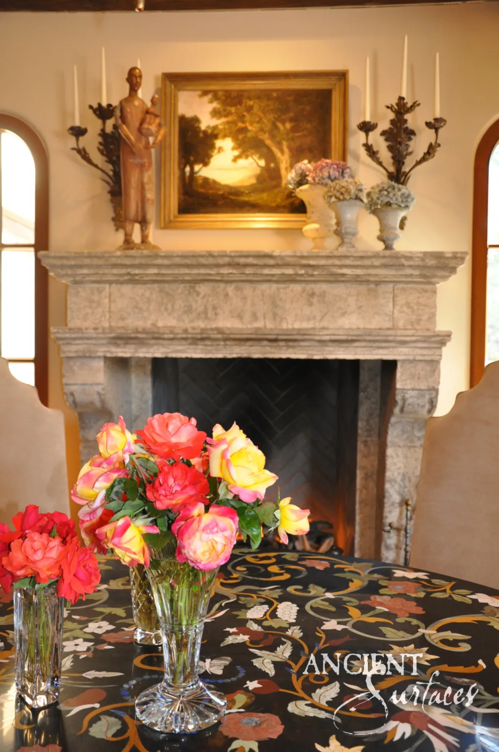 Restored antique limestone mantel with a weathered frieze and heavy cornice beneath a gilt framed landscape painting
