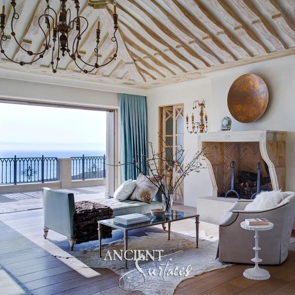 Limestone fireplace with scrolled jambs and a raised hearth in a living room whose glass doors fold open to an ocean terrace