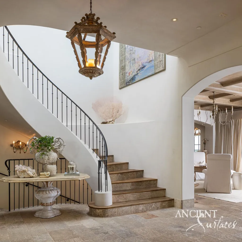 Limestone stair treads and risers curving up from an entrance hall beneath a carved lantern