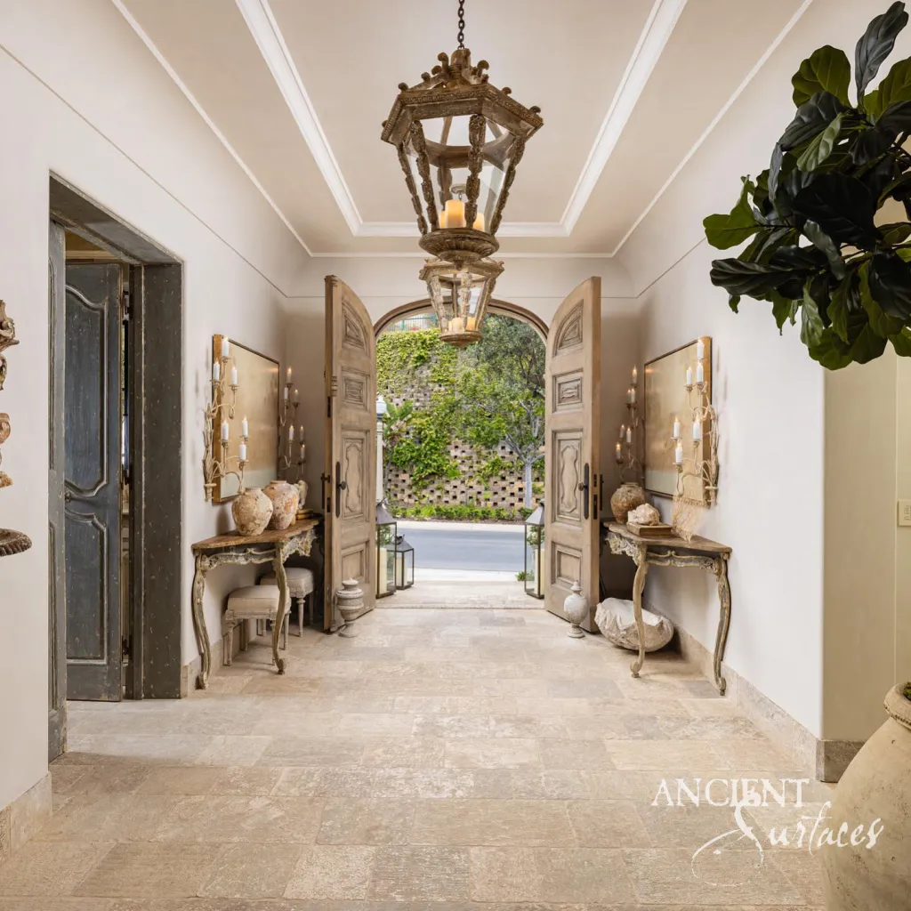 Stone floored entry hall seen from inside toward open double doors and a planted courtyard wall